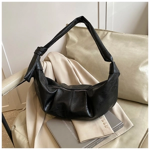 Detail of black pleated leather crescent bag with knot strap on a beige sofa