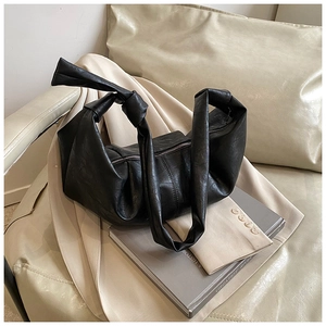 Detail of black pebbled leather dumpling bag featuring wide knotted shoulder strap and zipper