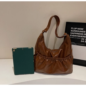 Nahaufnahme der braunen Hobo-Tasche mit Falten aus glänzendem Kunstleder und breitem Gurt