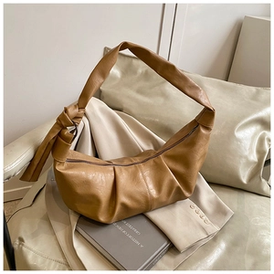 Close-up of caramel brown crescent shoulder bag with pleated texture and knotted strap detail
