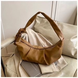 Detailed shot of caramel faux leather pleated bag with knot strap on a beige sofa