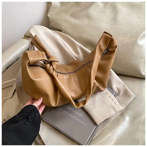Close-up of tan pleated leather dumpling bag featuring a unique knotted shoulder strap detail