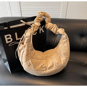Close-up of beige quilted crescent shoulder bag with pleated texture on black leather sofa