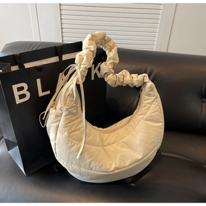Detail showing beige puffer bag with quilted pattern and scrunchie handle on a black sofa