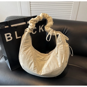 Detail of beige quilted crescent bag with ruffled handle on black leather sofa