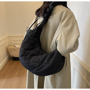 Detailed side view of a black quilted puffer bag on a model in a beige coat