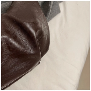 Detail shot of deep brown soft leather texture and elegant pleats on a slouchy hobo bag