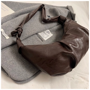 Detailed view of dark brown pleated croissant bag with knotted strap and metal ring
