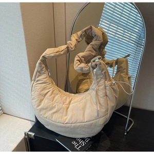 Detail of beige quilted puffer bag featuring a ruffled shoulder strap and side drawstring