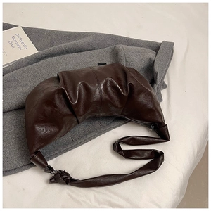Detail of a dark brown pleated crescent bag showing glossy leather texture and knotted strap