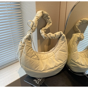 Detail of beige quilted crescent bag featuring ruffled strap and drawstring accents