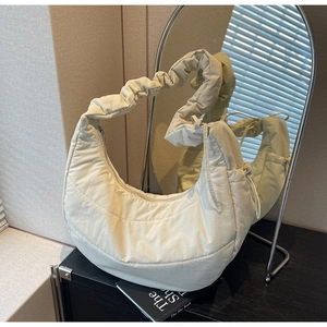 Detail of cream quilted puffer crescent bag featuring gathered ruched shoulder strap texture