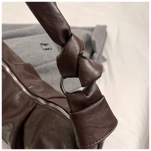 Detail of dark brown leather shoulder bag with knotted strap and silver ring buckle detail