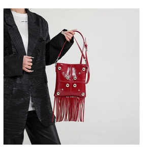 Detalle del bolso bandolera de charol rojo con tachuelas plateadas y flecos largos