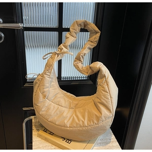 Detail of beige quilted crescent bag with ruffled shoulder strap and bow accent