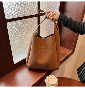 Detail of a brown faux suede shoulder bag featuring a slim buckle on a window background