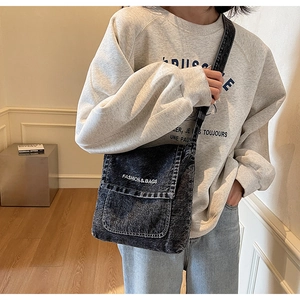 Dettaglio della borsa a tracolla in denim lavato con testo ricamato bianco sulla patta