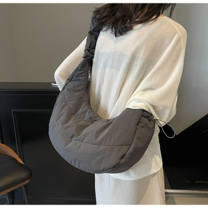Detailed view of dark grey quilted crescent bag with ruffled shoulder strap and zip closure