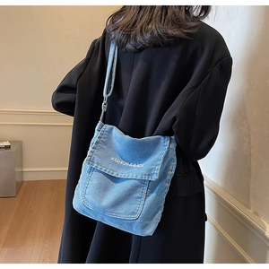 Dettaglio della borsa a tracolla in denim blu con ricamo indossata da un modello