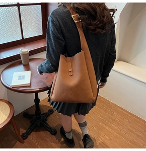 Brown matte PU leather bucket bag detail showing adjustable wide shoulder strap and gold buckle