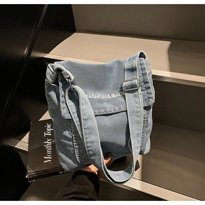 Dettaglio borsa a tracolla in denim blu con ricamo bianco e fibbia regolabile in metallo