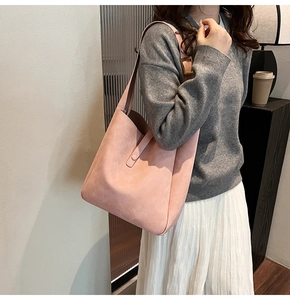 Soft pink suede shoulder bag shown on model with grey sweater and white pleated skirt