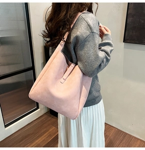 Detail of pink faux suede tote bag with decorative straps in minimalist indoor setting