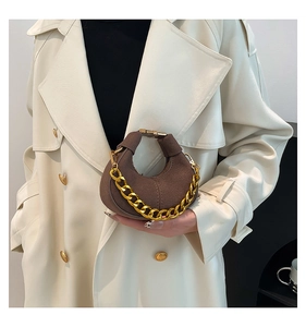Detalle de mini bolso de media luna en ante marrón con cadena dorada sostenido por mujer