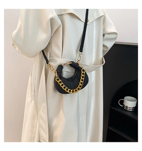 Detalle de un mini bolso de media luna negro con una cadena decorativa de metal dorado