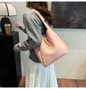 Close-up of pink suede hobo shoulder bag with wide strap and golden square buckle detail