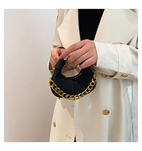 Detalle de un bolso de media luna en ante negro con cadena dorada llevado por una modelo