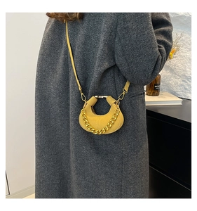 Detalle de bolso medialuna de cuero amarillo brillante con cadena dorada sobre abrigo