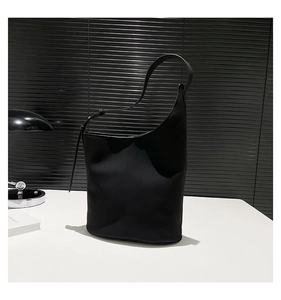 Detailed view of the asymmetrical curved rim and adjustable strap on this black leather bucket bag
