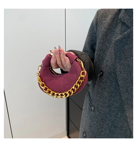 Detalle de bolso medialuna en ante granate con una cadena gruesa de metal dorado
