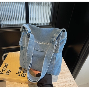 Dettaglio della borsa a tracolla in denim blu con ricamo bianco e tracolla regolabile