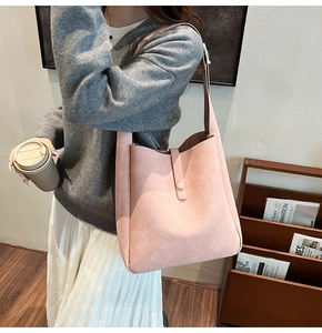 Detail view of pink suede shoulder bag featuring a minimalist bucket design and strap closure