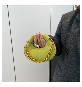 Bolso medialuna de ante verde lima con cadena dorada sobre un abrigo de lana gris