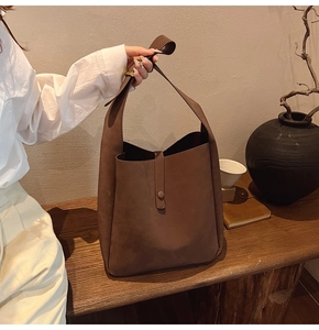 Detail of a deep brown suede tote bag with decorative buckle strap and matte leather texture