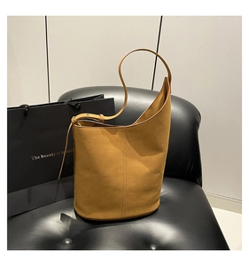 Detail of tan suede bucket bag with asymmetric curved opening and vertical stitching