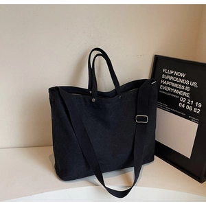Detail of black canvas tote bag showing thick texture, metal rivets and adjustable strap