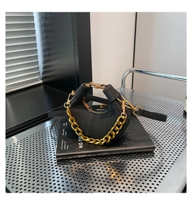 Detalle de un bolso de media luna negro con cadena dorada gruesa sobre fondo metálico