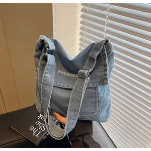 Dettaglio della borsa a tracolla in denim blu con scritte bianche e fibbia in metallo