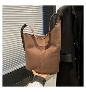 Detailed close-up of brown suede bucket bag featuring adjustable strap and bronze hardware