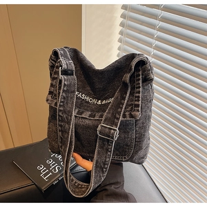Dettaglio della borsa a tracolla in denim nero lavato con ricami bianchi e fibbie metalliche