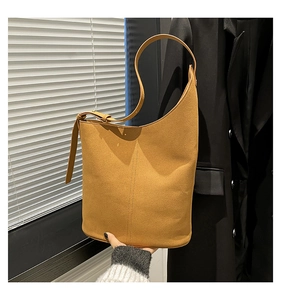 Close-up of minimalist camel bucket bag featuring asymmetric curved opening and suede texture