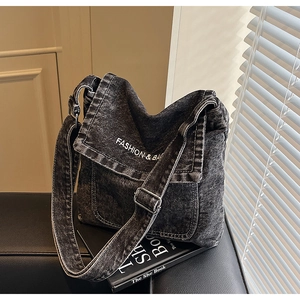 Dettaglio della trama denim lavato e della scritta bianca sulla borsa a tracolla nera