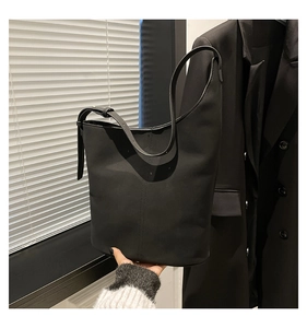 Detail view of black leather bucket bag with vertical stitching and adjustable strap