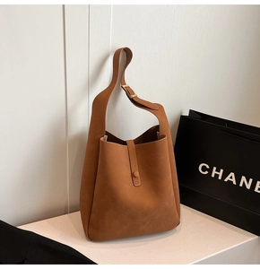 Detail of brown suede handbag featuring adjustable wide strap and metal buckle hardware