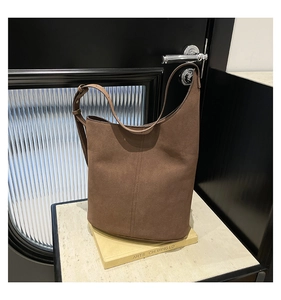 Detailed view of dark brown suede bucket bag with vertical stitching on stone base