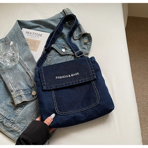 Dettaglio di una borsa a tracolla in denim blu scuro con logo bianco e fibbia in metallo